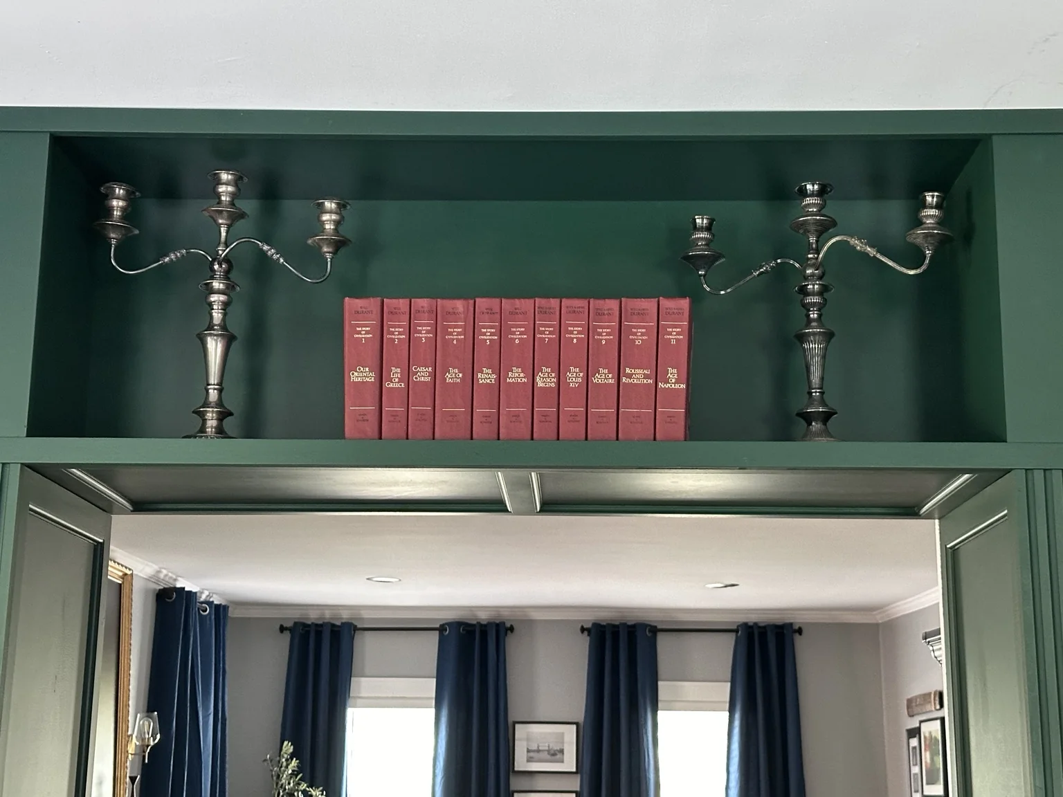 Upper library shelf styled with red books and metal candelabras