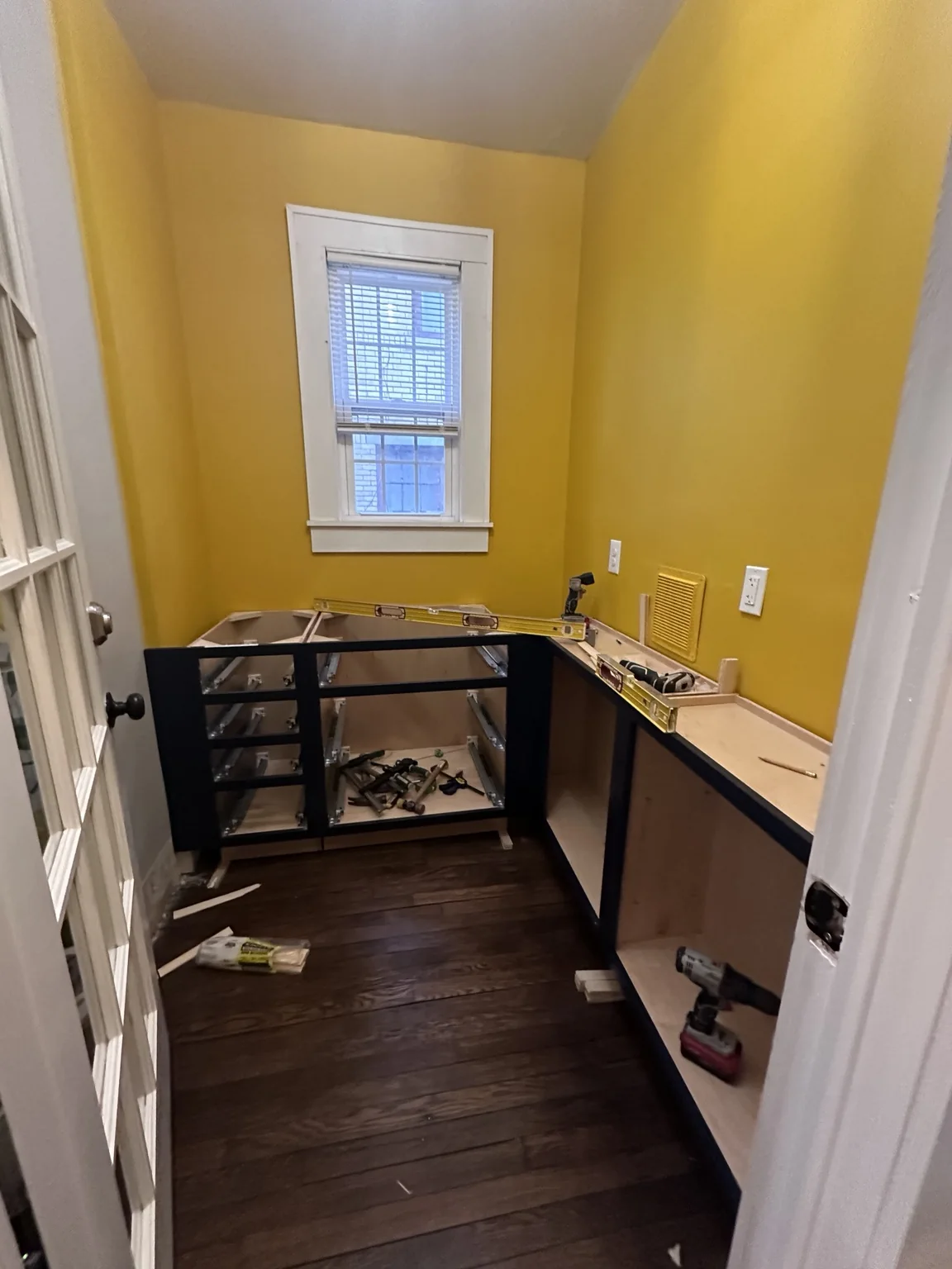 Dark pantry cabinet boxes being installed against the yellow walls